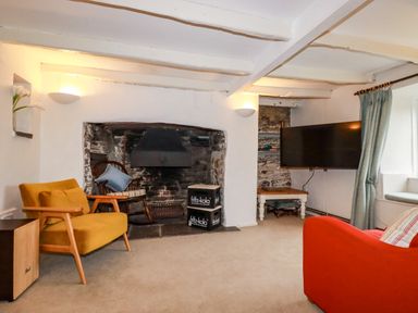 A living room with chairs a fireplace and a television at Lanvean Farmhouse in Lanvean near St Mawgan