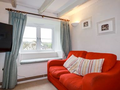 A living room with a red sofa and striped pillows next to a window with blue curtains at Lanvean Farmhouse in Lanvean near St Mawgan