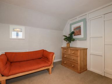 A room with an orange cushioned wooden sofa a wooden chest of drawers with a plant on top and two framed pictures on the walls at Lanvean Farmhouse Lanvean near St Mawgan
