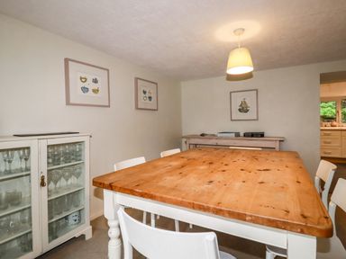 A dining room with a large wooden table white chairs a glass cabinet with glasses and framed pictures on the wall at Lanvean Farmhouse Lanvean near St Mawgan