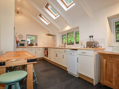 A kitchen with wooden table and stools white cabinets and appliances under skylights at Lanvean Farmhouse Lanvean near St Mawgan