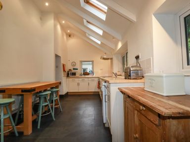 A kitchen with a wooden table and stools a countertop with a toaster and cabinets under skylights at Lanvean Farmhouse in Lanvean near St Mawgan