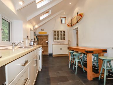 A kitchen with wooden countertops white cabinets a wooden table with stools and a surfboard on the wall at Lanvean Farmhouse Lanvean near St Mawgan
