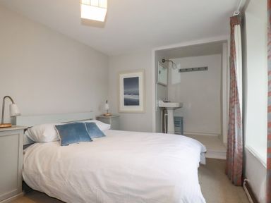 A bedroom with a double bed blue pillows bedside tables lamps a wall mirror and a small sink at Lanvean Farmhouse Lanvean near St Mawgan