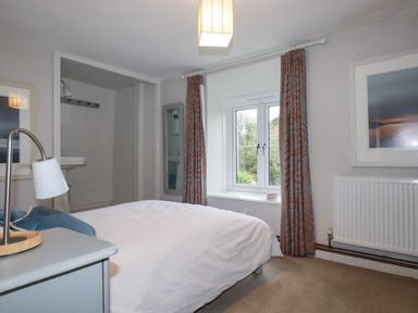 A bedroom with a bed white bedding a bedside table with a lamp window with curtains a radiator and framed pictures at Lanvean Farmhouse Lanvean near St Mawgan