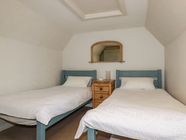 A bedroom with two single beds and a wooden nightstand with a mirror above at Lanvean Farmhouse Lanvean near St Mawgan