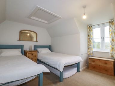 A bedroom with two single beds a wooden nightstand a wall mirror a window with patterned curtains and a wooden chest at Lanvean Farmhouse in Lanvean near St Mawgan