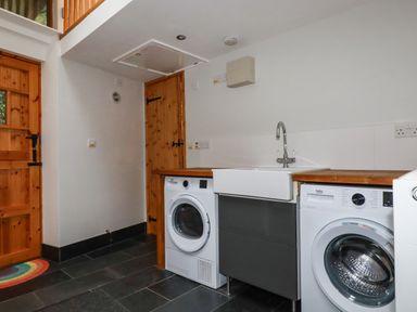 A utility room with washing machine and dryer under wooden countertops and a sink with faucet at Lanvean Farmhouse Lanvean near St Mawgan