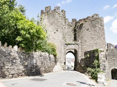 A stone castle gate with round towers and an archway over a road surrounded by stone walls and greenery at Coed Derw Isaf in Betws-Y-Coed