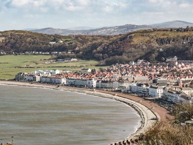 A seaside town with a curved promenade along the coast and houses on hills behind the shore at Coed Derw Isaf in Betws-Y-Coed