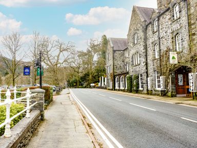 A street with a stone building labeled royal oak hotel and a sidewalk with railings and trees at Coed Derw Isaf in Betws-Y-Coed