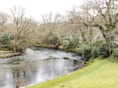 A river flowing through a wooded area with trees and grass on the banks at Coed Derw Isaf in Betws-Y-Coed