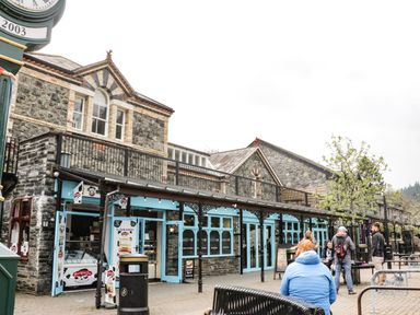 A street view of a stone building with blue shop doors and windows and people standing and sitting nearby at Coed Derw Isaf in Betws-Y-Coed