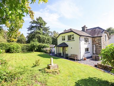 A garden with grass and trees next to a white house with a stone extension at Coed Derw Isaf in Betws-Y-Coed