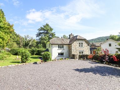 A stone and white painted house with a gravel driveway and garden at Coed Derw Isaf in Betws-Y-Coed