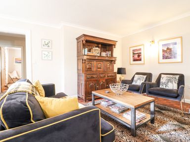 A living room with black and yellow cushions on a sofa two armchairs a wooden coffee table and a wooden cabinet at Coed Derw Isaf in Betws-Y-Coed