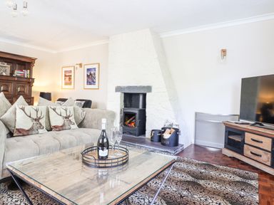 A living room with a sofa with deer cushions a glass coffee table a fireplace a TV and wooden furniture at Coed Derw Isaf in Betws-Y-Coed
