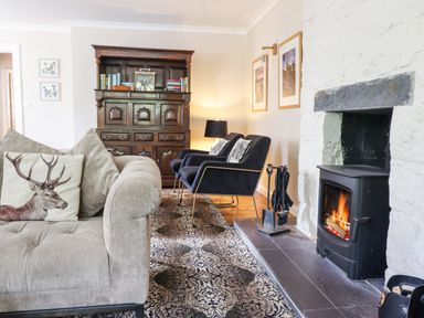 A living room with a beige sofa and deer cushion blue armchairs fireplace and wooden cabinet at Coed Derw Isaf in Betws-Y-Coed