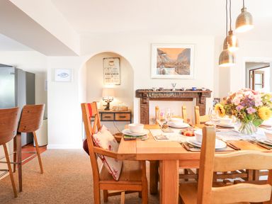 A dining room with a wooden table set with plates glasses and cutlery a flower vase on the table wooden chairs a fireplace with cups on the mantel and pendant lights above the table at Coed Derw Isaf in Betws-Y-Coed