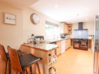 A kitchen with wooden cabinets, a black oven, a window above the sink, and two bar stools at a countertop at Coed Derw Isaf in Betws-Y-Coed