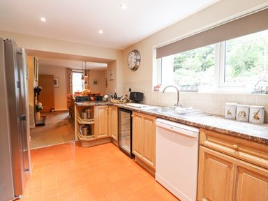 A kitchen with wooden cabinets white dishwasher and a large window overlooking greenery at Coed Derw Isaf in Betws-Y-Coed
