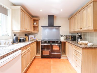 A kitchen with wooden cabinets black stove and various appliances at Coed Derw Isaf in Betws-Y-Coed