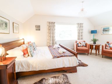A bedroom with a wooden bed table and two armchairs near a window at Coed Derw Isaf in Betws-Y-Coed