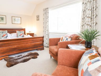 A bedroom with a wooden bed and two armchairs with a plant on a side table at Coed Derw Isaf in Betws-Y-Coed