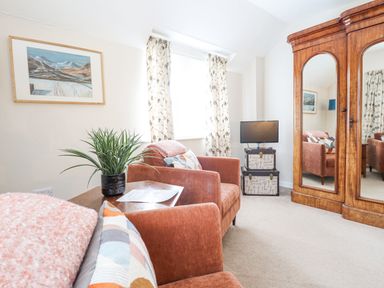 A sitting room with armchairs a wooden wardrobe with mirrors a small television on stacked trunks and a plant on a side table at Coed Derw Isaf in Betws-Y-Coed