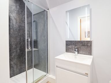 A bathroom with a glass-enclosed shower and a white sink with a mirror above at Coed Derw Isaf in Betws-Y-Coed