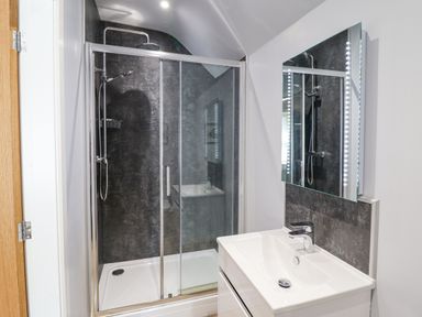 A bathroom with a glass shower enclosure and a white sink with a mirror at Coed Derw Isaf in Betws Y Coed
