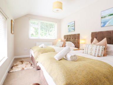 A bedroom with two single beds with yellow blankets and rolled towels at Coed Derw Isaf in Betws-Y-Coed