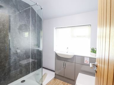 A bathroom with a walk-in shower a sink with storage cabinets and a window at Coed Derw Isaf in Betws-Y-Coed