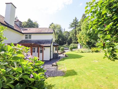 A white house with a garden and lawn surrounded by trees at Coed Derw Isaf in Betws-Y-Coed