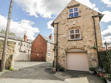 A stone house with a closed garage door surrounded by potted plants and neighboring brick and stone buildings