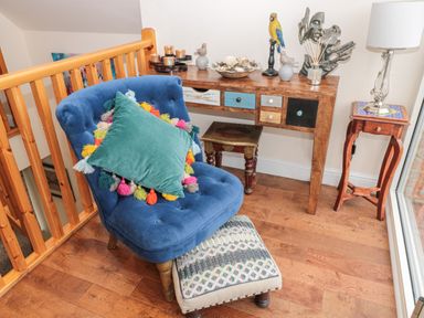 A blue chair with a colorful pillow and footstool next to a wooden table with drawers and decorative items at River Cottage in Morpeth