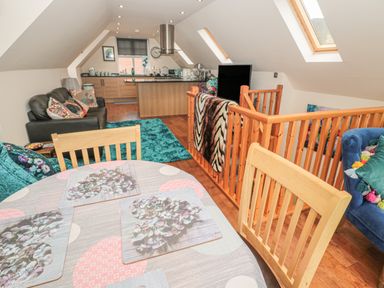 An open plan living area with a dining table and chairs a sofa a kitchen island and wooden staircase at River Cottage in Morpeth