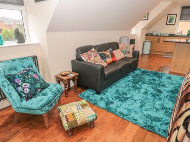 A living room with a black sofa with pillows a turquoise chair and rug and wooden floor at River Cottage in Morpeth