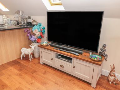 A television on a wooden stand with remote controls and decorative items on and around the stand at River Cottage in Morpeth