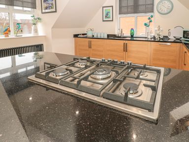 A kitchen with a gas stove on a black countertop wooden cabinets and windows with decorations at River Cottage in Morpeth