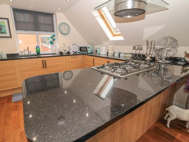 A kitchen with black countertops a gas stove wooden cabinets a skylight window and various kitchen appliances at River Cottage in Morpeth
