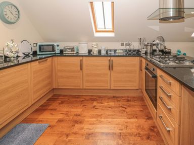 A kitchen with wooden cabinets black countertops a gas stove an oven a blue microwave a blue toaster a wall clock and a skylight window at River Cottage in Morpeth