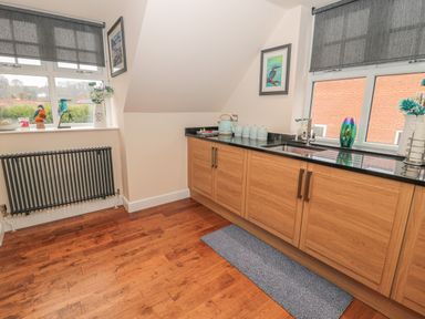 A kitchen with wooden cabinets black countertop two windows with blinds and a radiator at River Cottage in Morpeth