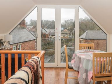 A dining area with wooden chairs and a table covered with a polka dot tablecloth next to large glass doors showing rooftops at River Cottage in Morpeth