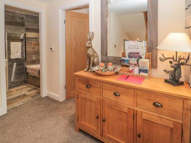 A hallway with a wooden cabinet a mirror a lamp a rabbit figurine and an open door showing a bathroom at River Cottage in Morpeth