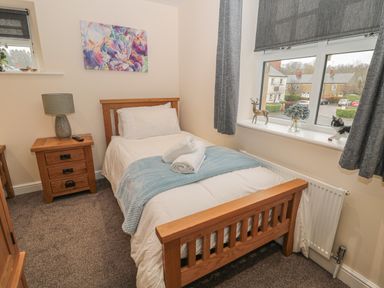 A bedroom with a wooden single bed next to a window with gray curtains and a bedside table with a lamp at River Cottage in Morpeth