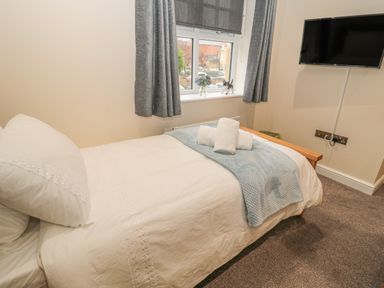 A bedroom with a single bed white bedding a blue blanket a window with gray curtains and a wall mounted television at River Cottage in Morpeth