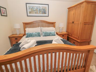 A bedroom with a wooden bed frame, two bedside tables with lamps, a wooden wardrobe, and framed flower pictures on the walls at River Cottage in Morpeth