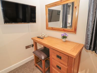 A wooden dressing table with a mirror a small flower pot and a TV mounted on the wall at River Cottage in Morpeth