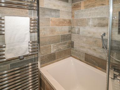 A bathroom corner with a white bathtub tiled walls and a metal towel rack holding a white towel at River Cottage in Morpeth